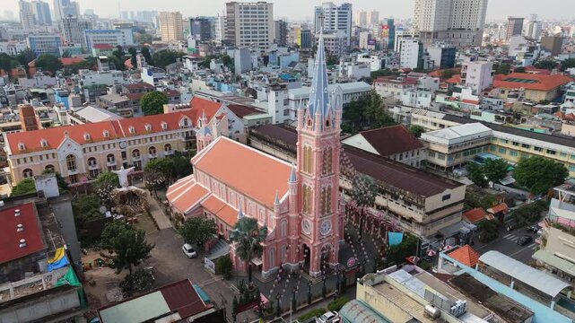 Cinematic aerial view of Tan Dinh Pink Church in Ho Chi Minh City, Vietnam. Iconic pink cathedral surrounded by urban skyline and dense city architecture in Southeast Asia.