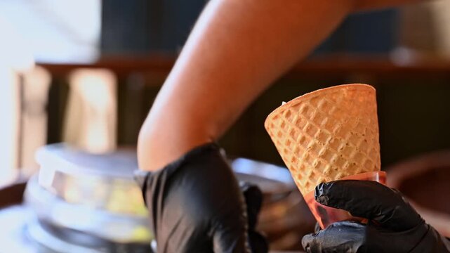 Hands of an ice cream vendor serving scoops of ice cream into an ice cream cone