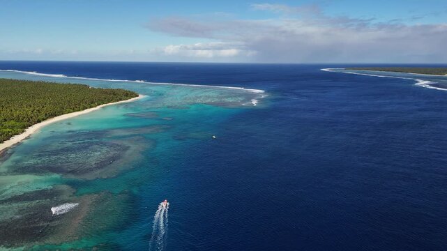 Drone orbit around Eua Island, Kingdom of Tonga, sweeping above coral reefs as a small speedboat cuts across turquoise water, leaving a bright foamy trail through the untouched Pacific paradise.