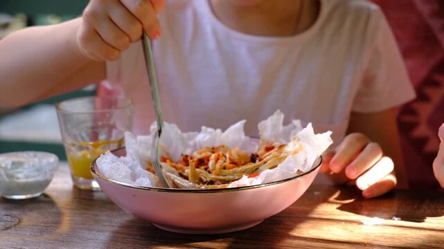 Child girl eating spicy salad with seafood, fuzhou, squid, mix vegetables, peanut, sesame, mushroom, crispy puffed rice. Vacations and having lunch in the terrace of guest house hotel.