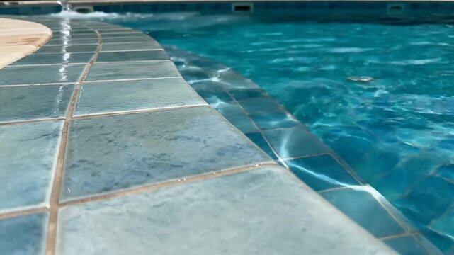 Refreshing close-up shot of blue pool tiles and sparkling water ripples, perfect for luxury travel promotions or summer vacation advertisements.