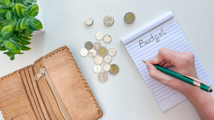 A hand records expenses in a notebook labeled 