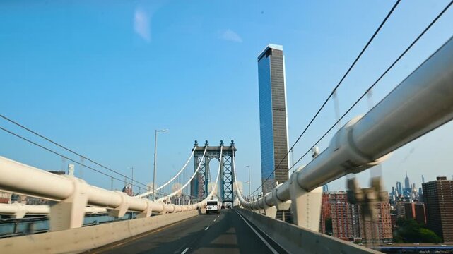 New York, USA, 5 August 2025: View of Manhattan Bridge tower and tall skyscraper. Moving vehicle perspective of bridge structure and a modern high rise building.