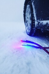 Automotive Jumper Cables in Snow Beside Car Tire Prepared for Roadside Assistance and Emergency Repair During Winter Storm with Glowing Power Indicators