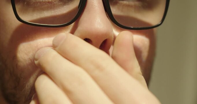 Close-up of a man wearing glasses wiping white powder from under his nose, creating an ambiguous scene that can symbolize substance use, hygiene, or suspicious behavior.