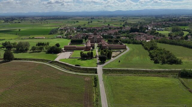 Chignolo village and the historic Procaccini Castle complex appear surrounded by farmland, hedgerows, and scattered houses in flat Po Valley plain of Lombardy, Pavia, Italy, drone establishing shot