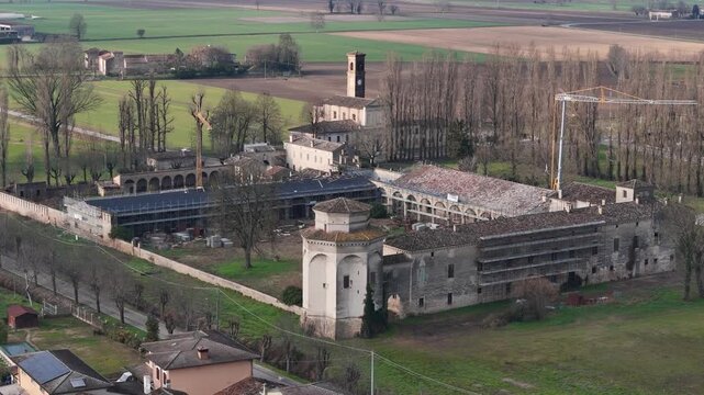Aerial view of the historic Casatico Corte Castiglione rural court complex surrounded by Po Valley farmland, showing scaffolding, roof restoration works, courtyards, arcades and winter trees