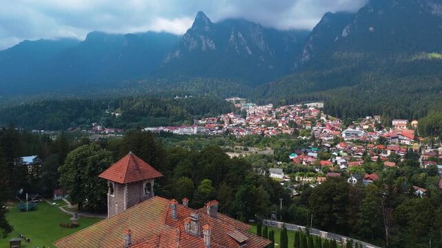 Drone shot moving toward the tower of Cantacuzino Castle, revealing the town of Busteni and the Bucegi Mountains in the background.