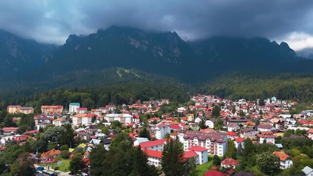 Drone advances over Bușteni with forest and Bucegi Mountains behind