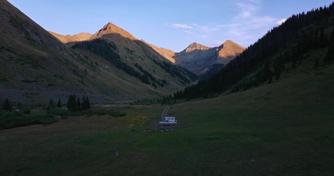 Golden hour aerial of alpine valley with dirt road and camper at dusk, alpenglow, Trans America Trail, Colorado, USA
