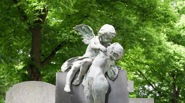 Zentralfriedhof cemetery pan across gravestone and angel statue among lush green trees, historic memorial sculpture in Vienna, Austria. Calm, reflective summer atmosphere.