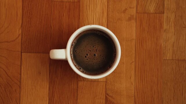 Top-down view of freshly brewed black coffee in a white ceramic cup placed on a warm wooden surface. Minimal composition, cozy mood, and everyday lifestyle atmosphere suitable for morning routines, ca