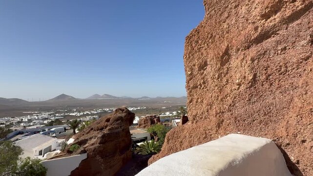 Scenic View of Lagomar Lanzarote Canary Islands with White Buildings Palm Trees Volcanic Rock Formations and Distant Mountains Under a Clear Blue Sky on a Sunny