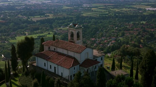 Aerial view of Montevecchia church in Lombardy Italy featuring red tile roofs and a bell tower The church is surrounded by green trees and rolling hills in the Italian countryside.