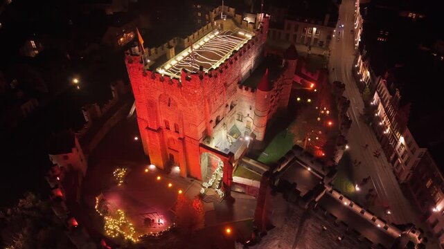 Aerial capture of the illuminated Gravensteen Castle in Ghent, showcasing its medieval architecture and dramatic presence within the city at night.