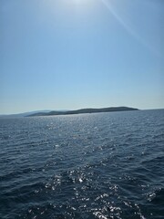 Naklejka premium Sparkling blue ocean water with sun glint and distant island silhouette