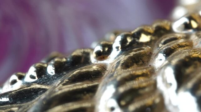 The scene shows a shiny metallic object with a detailed, textured surface laid out on a colorful backdrop. Light reflects off the object, highlighting its features.