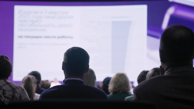 conference audience watching large data slide, rear silhouettes focus on projected chart and statistics, analysts and managers reviewing metrics, dim purple