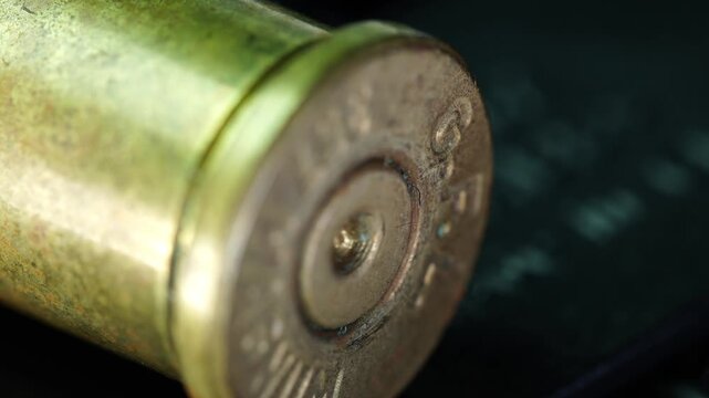 The image shows a close-up view of a spent bullet casing resting on a dark surface. Details of the casing are clear, showing markings and wear from use.