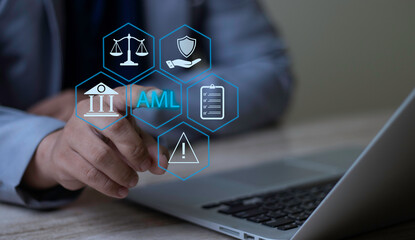 Businessman using laptop pointing at AML (Anti-Money Laundering) hologram with law scales, bank, and compliance checklist icons. Concept of preventing financial crime and regulatory compliance.