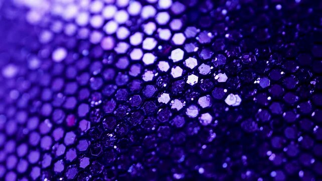 Close look at sequins showing bright purple colors and shiny textures under light in a dark setting. This takes a close view of sequins with bright purple colors. The light reflects off the shiny sun.