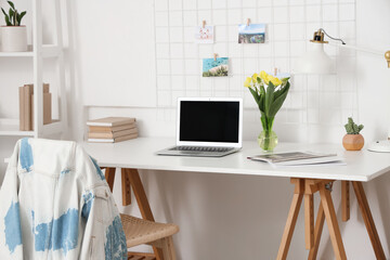 Blank laptop and vase with flowers on desk in office