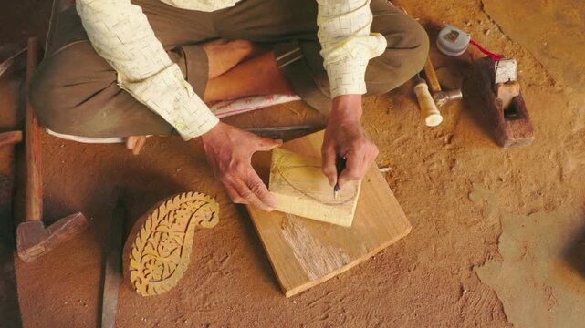 Traditional Indian Artisan Hand-Carving Wooden Printing Blocks in a Rural Workshop - Top-Down View of a Craftsman Sketching a Paisley Design for Textile Printing