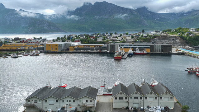 12 july 2025, Hus&oslash;y, Norway. Aerial, drone view of harbor in  village Husoy and island in &Oslash;yfjorden fjord during sunset. Ships, fishing industry, packhouses. Beautiful nature, mountains surrounding fj
