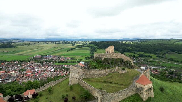 Aerial drone footage of Rupea Fortress, Romania, revealing medieval stone walls, rolling green hills and the historic town below. Cinematic landscape, travel and heritage concept.