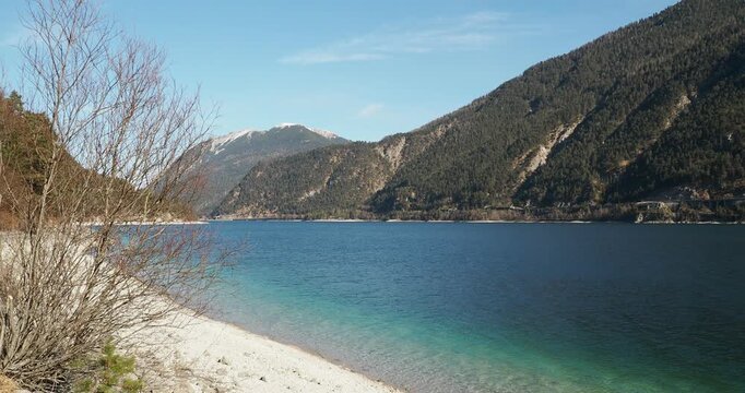 Lake Achen in the heart of Tyrol surrounded by mountains, the slopes of the Klobenjoch to the east followed by the snow-capped peaks of Unnutz to the north above Achenkirch