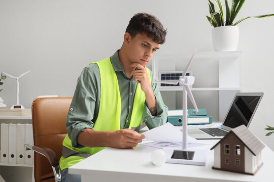 Male engineer with diagrams and wind turbine model working at table in office