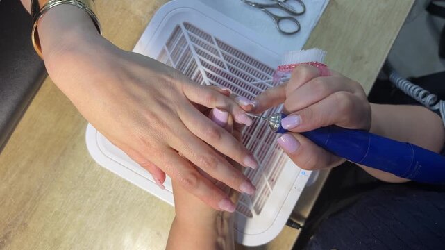Manicurist using electric nail drill on client's fingernails
