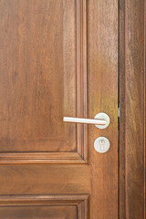 A brown wooden door with polished alloy material doorknob handle of the domestic room, close-up and...