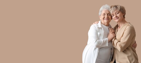 Happy woman and her senior mother hugging on beige background with space for text