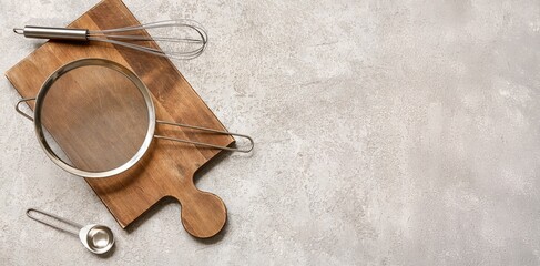 Wooden board with metal sieve, whisk and scoop on grey grunge background with space for text