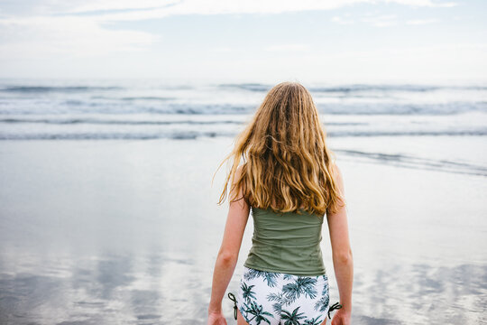 Teen girl with long blond hair walking towards ocean in swimsuit