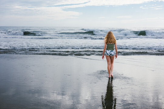 Young teen girl walking into ocean waves in swimsuit