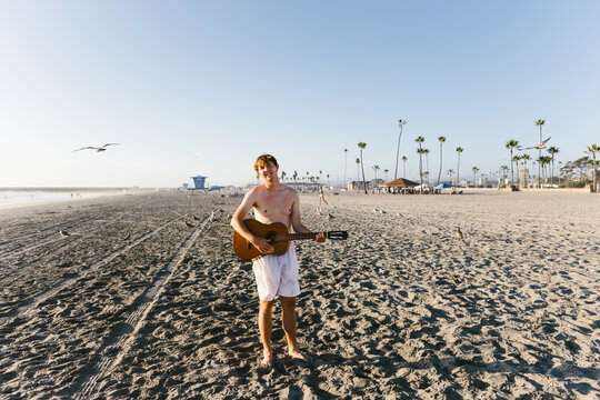 Young adult boy with guitar smiling on beach in sunshine