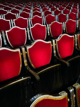 Empty red theater seats arranged in rows inside auditorium. Perspective view with repeating pattern and symmetry. Concept of cinema, concert, performance, audience, and entertainment venue interior.