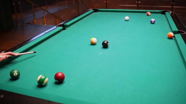 Wide view of pool table in a bar with scattered balls and player cue after a missed shot, green felt background and copy space for leisure, competition, and nightlife concepts.
