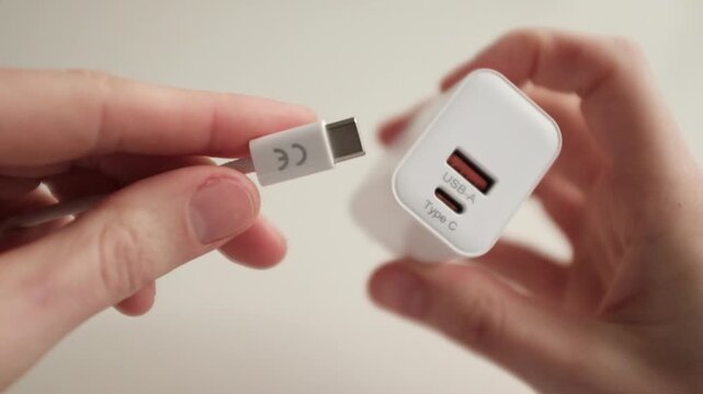 Close-up video of a white USB-C power adapter and charging cable being handled by a person against a clean, neutral background. Compact design, port details, and the connector of high-speed charging.