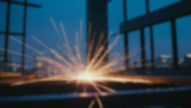 Blurred background of Steel moment frame welded connection with thick flange plates, continuity plates and stiffeners clearly visible, active arc welding producing bright sparks and molten metal.