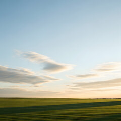 Obraz premium Vast Landscape Under a Calm Sky: A panoramic vista unfolds, where a boundless expanse of green fields meets a serene sky adorned with scattered, fluffy clouds.