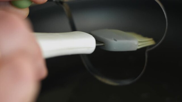 Person anoints the stainless heart shaped egg ring with oil