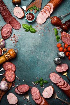 Assortment of different types of salami, paperoni and smoked sausages cut into slices on a dark stone table. Concrete background. Top view.