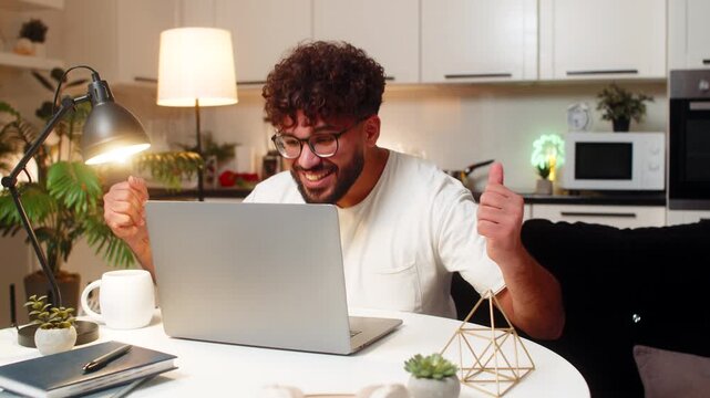 Arabian man at home opens laptop sees approved grant message wins application feels joy. Egyptian guy sitting at table reads good news alert about win and jackpot style reward celebrates success.