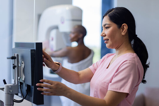Female tech in pink scrubs and patient having mammogram in clinic, using monitor, copy space
