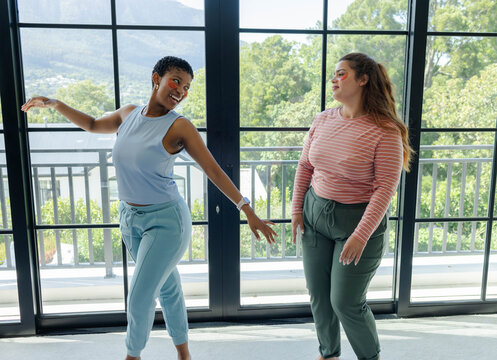 Two women are dancing near floor-to-ceiling window panels with balcony railing, face paint