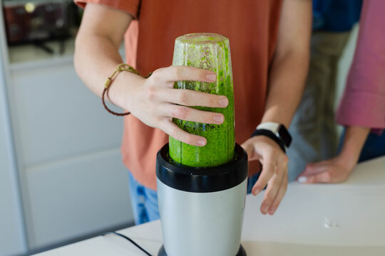 Parent in pink top leaning, adolescent male in rust shirt holding inverted cup of green puree