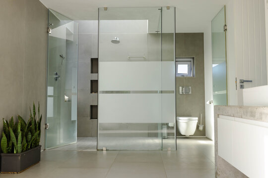 Frameless glass shower enclosure showing frosted wide bands and rain showerhead in modern bathroom